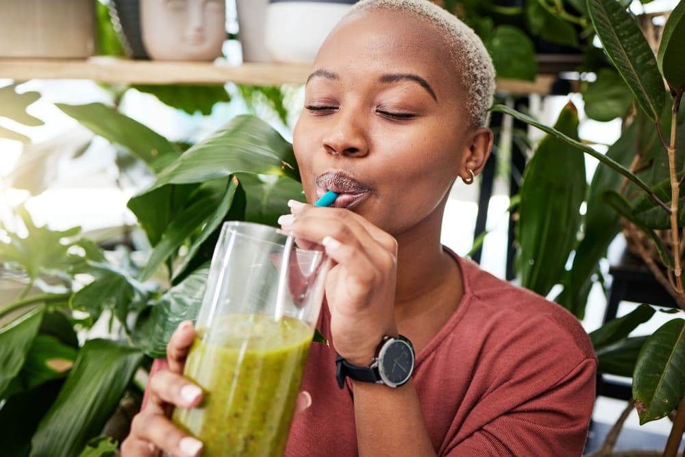 Kobieta pije koktajl warzywny z dodatkiem spiruliny. 