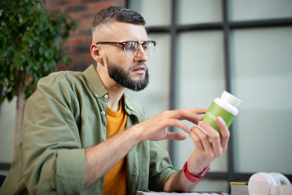 Mężczyzna trzyma w rękach suplement diety ze spiruliną i czyta, jak należy go prawidłowo stosować. 